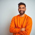 Young indian man wearing orange sweater over isolated white background happy face smiling with crossed arms looking at the camera. Positive person.